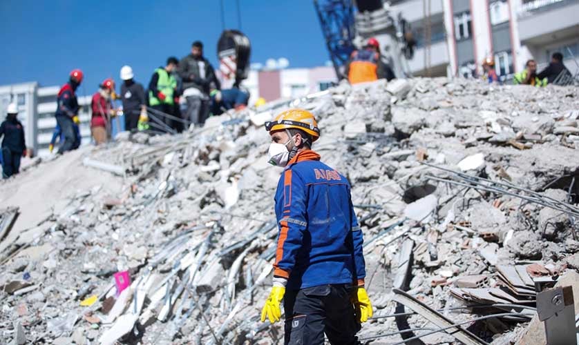 Un rescatador con un casco y mascarilla busca sobrevivientes en los escombros en Turquía tras el terremoto. Al fondo se ven otros rescatadores trabajando.