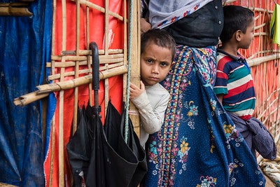 Child peering at camera next to standing mother and another child looking away. Child peering at camera next to standing mother and another child looking away.