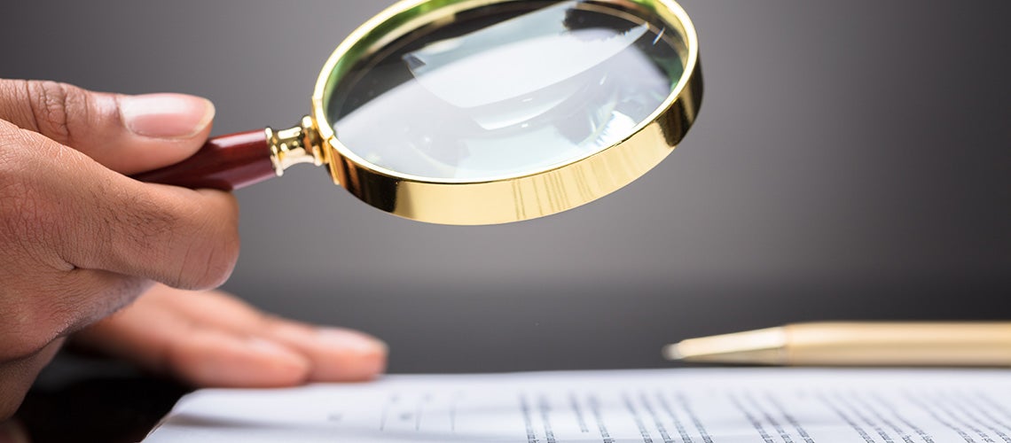 Close-up of a hand looking at a document with magnifying glass | © shutterstock.com
