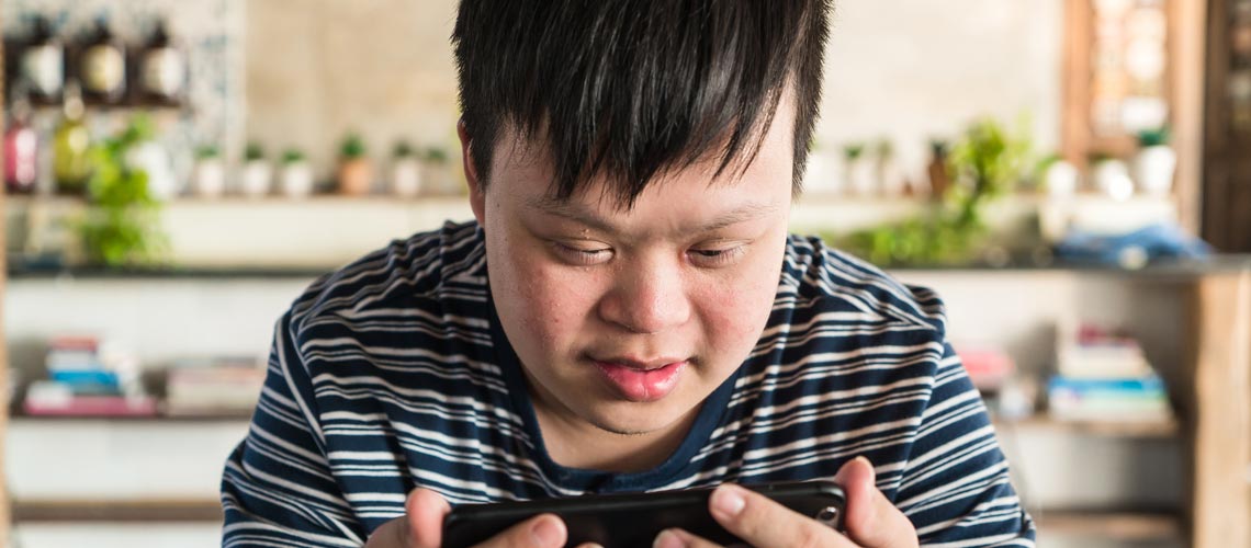 Un niño con síndrome de Down mira un teléfono inteligente. Fotografía: © Shutterstock Un niño con síndrome de Down mira un teléfono inteligente. Fotografía: © Shutterstock