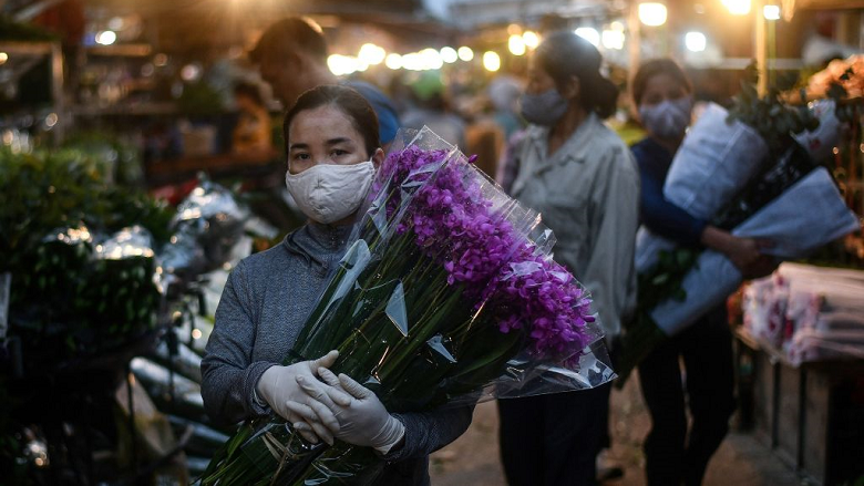 A woman wearing a face mask amid concerns over the spread of COVID-19 (coronavirus) carries flowers at the Quang Ba flower market in Hanoi at dawn on May 11, 2020. (Photo by MANAN VATSYAYANA/AFP via Getty Images)