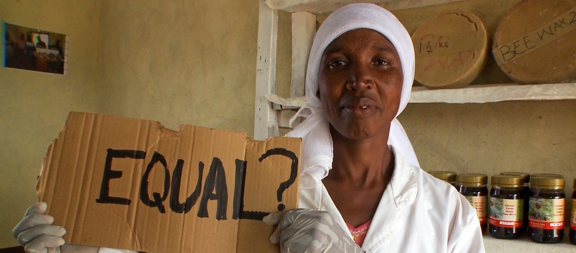 Woman honey producer from Kenya holding a sign that reads "Equal?"