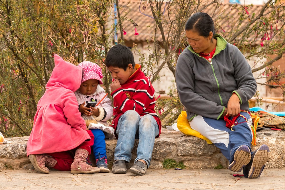 Woman sitting with her children playing with a phone in rural Peru. Credit: nmessana/iStock