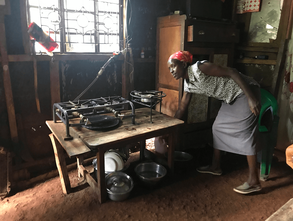 A Kenyan woman in her kitchen bends downs to use a biogas-burning stove