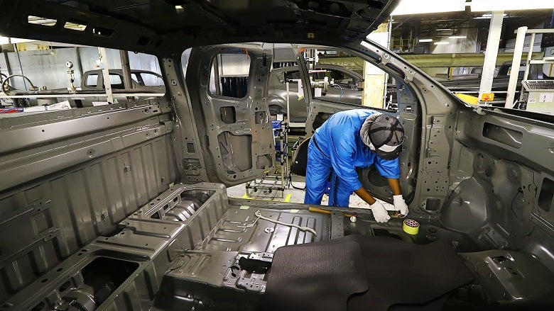 An auto worker working on the body work of an unpainted vehicle.