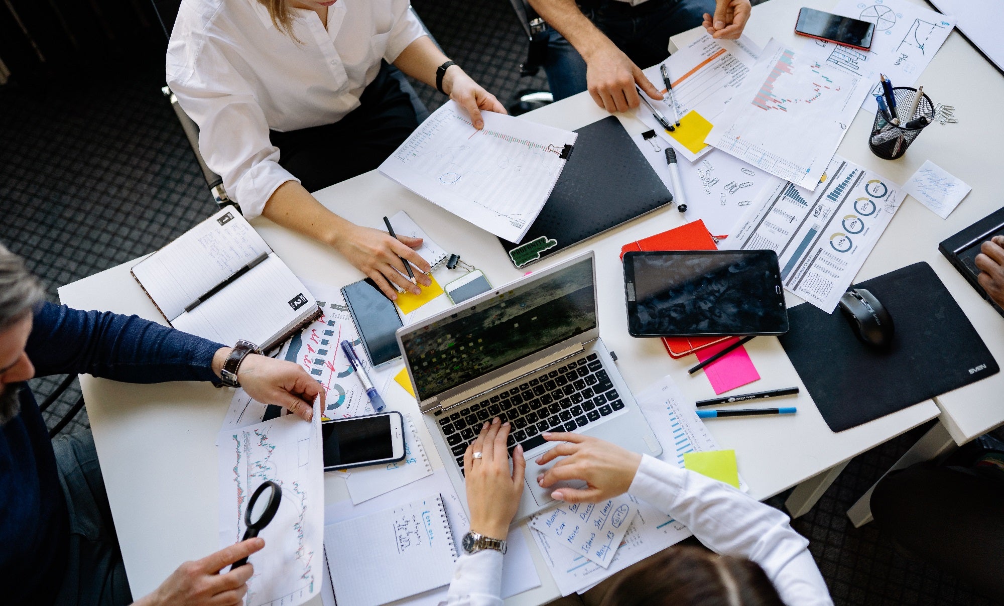 A group of working together, looking over papers at a table. Shown from above, with faces omitted