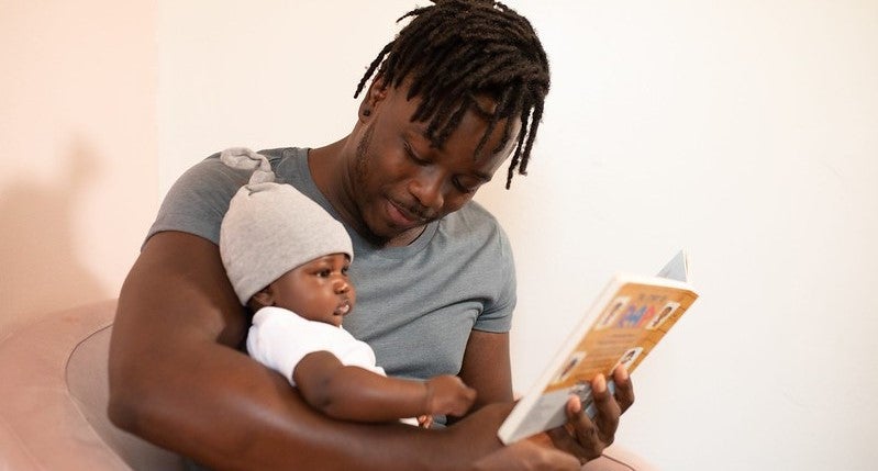 A photo of a man reading to an infant. A photo of a man reading to an infant.