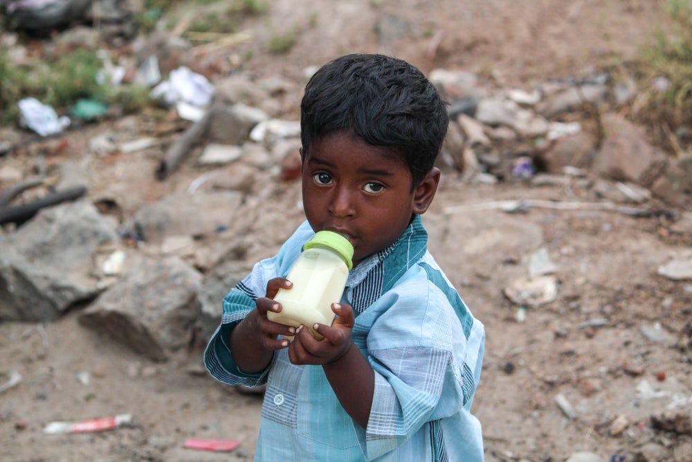 Homeless and poor child drinking milk, representing the situation of children in India who do not have access to a home, nutrition or education. 