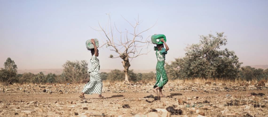 Two young girls carry containers of fresh water across dry land. Two young girls carry containers of fresh water across dry land.