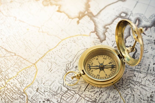 Retro styled golden compass (sundial) and old white nautical chart close-up.