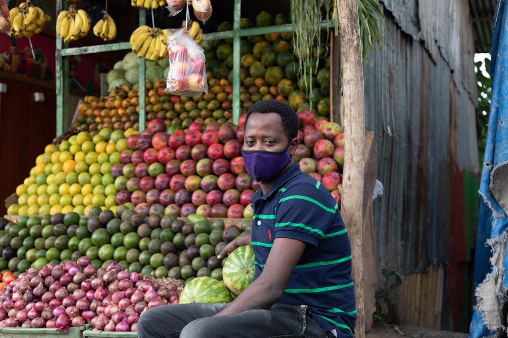 Addis Ababa / Ethiopia - June 14 2020: Fruit Seller sitting, waiting for customers during COVID-19 pandemic. Working while wearing a mask. ©Alazar Kassa/Shutterstock