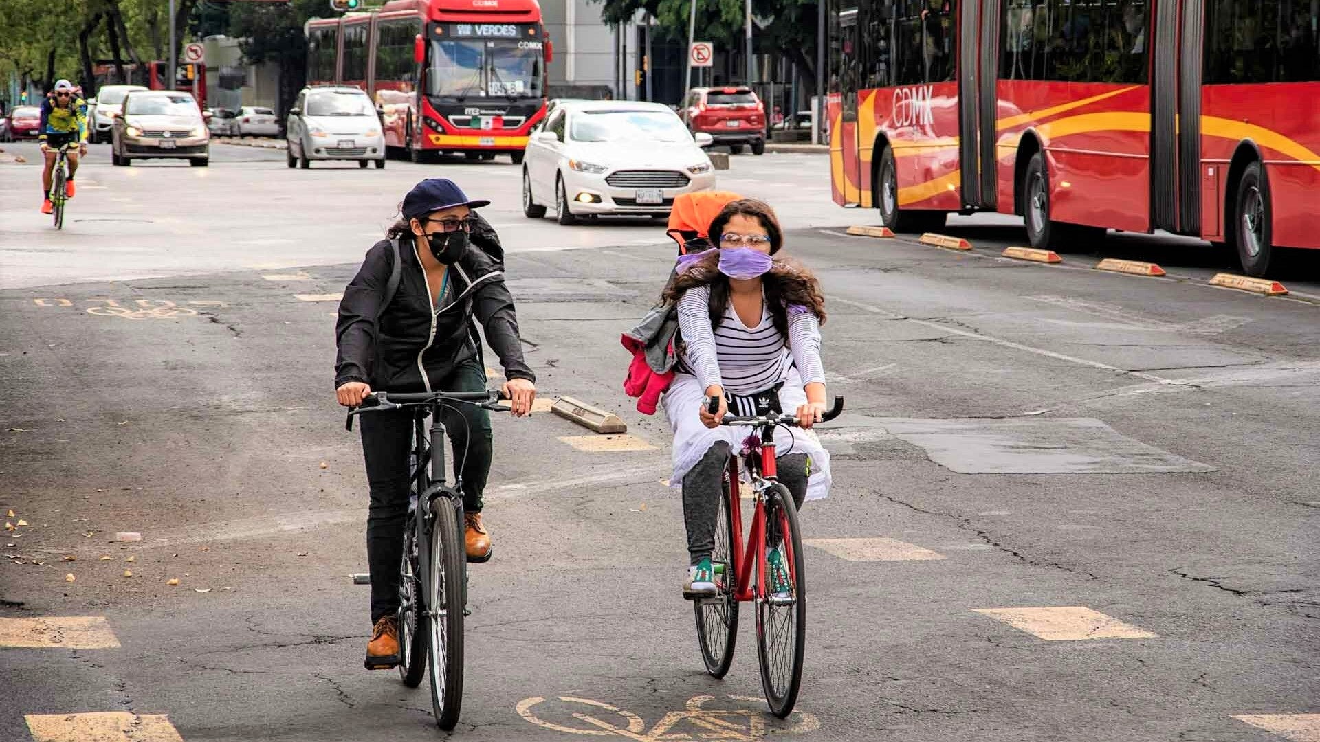 A couple of women riding bikes in the avenue next to the metrobus in Mexico City