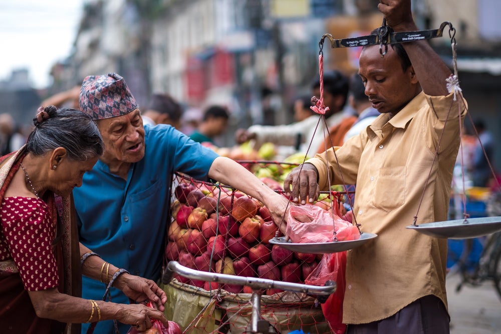 Nepalese man weighs up apples for older people on the local street market in Kathmandu, Nepal. Photo: Shutterstock