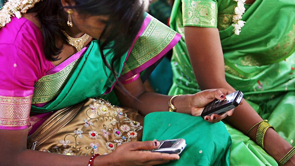 Young women look at their mobile phones during a community meeting in India. © Simone D. McCourtie/World Bank